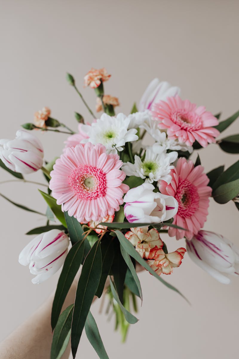 Beautiful floral bouquet featuring pink gerberas, white tulips, and greenery on a beige background.
