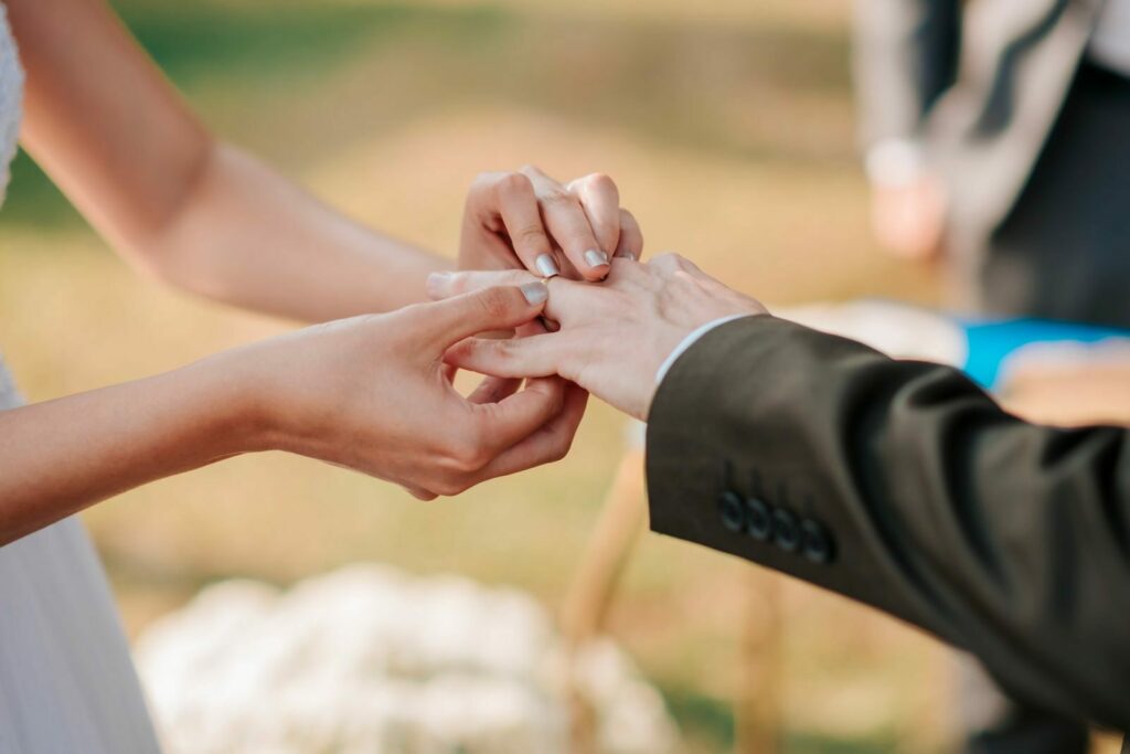 Close-up of a couple exchanging wedding rings during an outdoor ceremony.