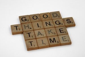 Close-up of wooden tiles spelling 'Good Things Take Time' on a white background.