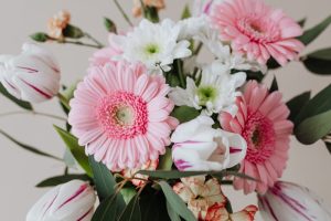 Beautiful floral bouquet featuring pink gerberas, white tulips, and greenery on a beige background.